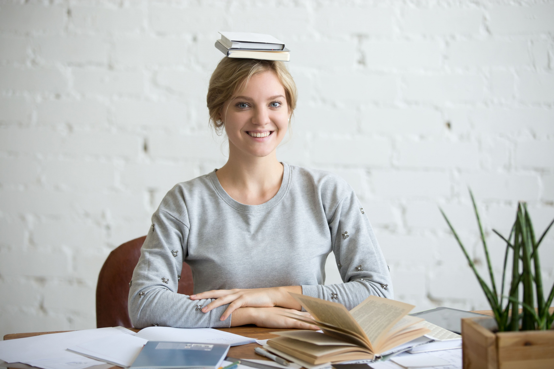 portrait-of-smiling-woman-at-desk-books-on-her-head.jpg