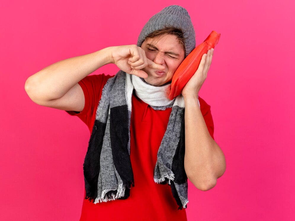 young-handsome-blonde-ill-man-wearing-winter-hat-scarf-touching-face-with-hot-water-bottle-wiping-nose-with-finger-with-closed-eyes-isolated-crimson-background-with-copy-space_141793-77913.jpg