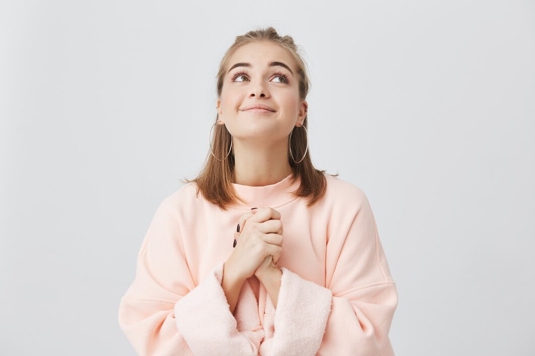 waist-up-portrait-cheerful-caucasian-female-with-fair-hair-posing-studio-with-looking-upwards-girl-dressed-pink-sweatshirt-keeping-palms-pressed-together-having-begging-look_176420-13506.jpg